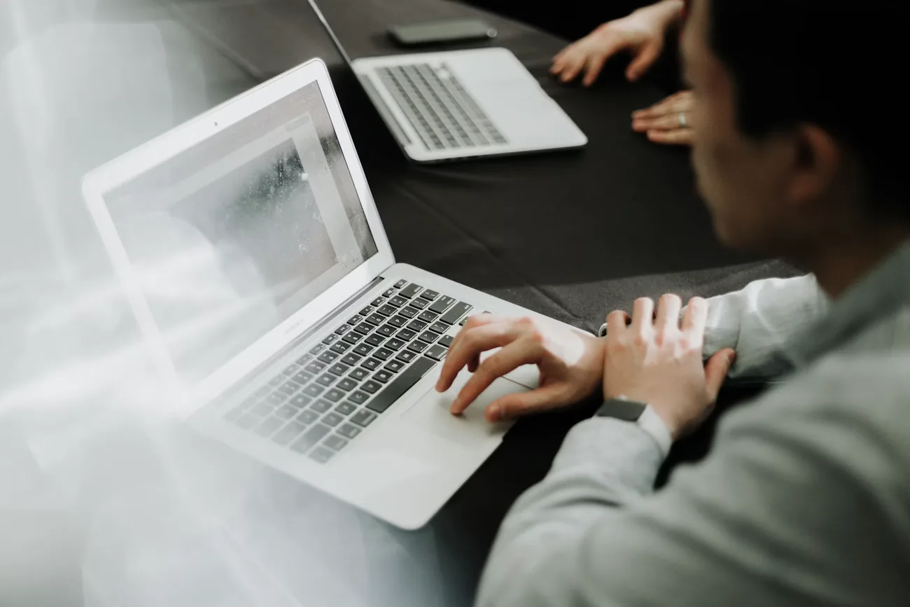 Zwei Personen arbeiten gemeinsam an Laptops an Transaktionsunterlagen